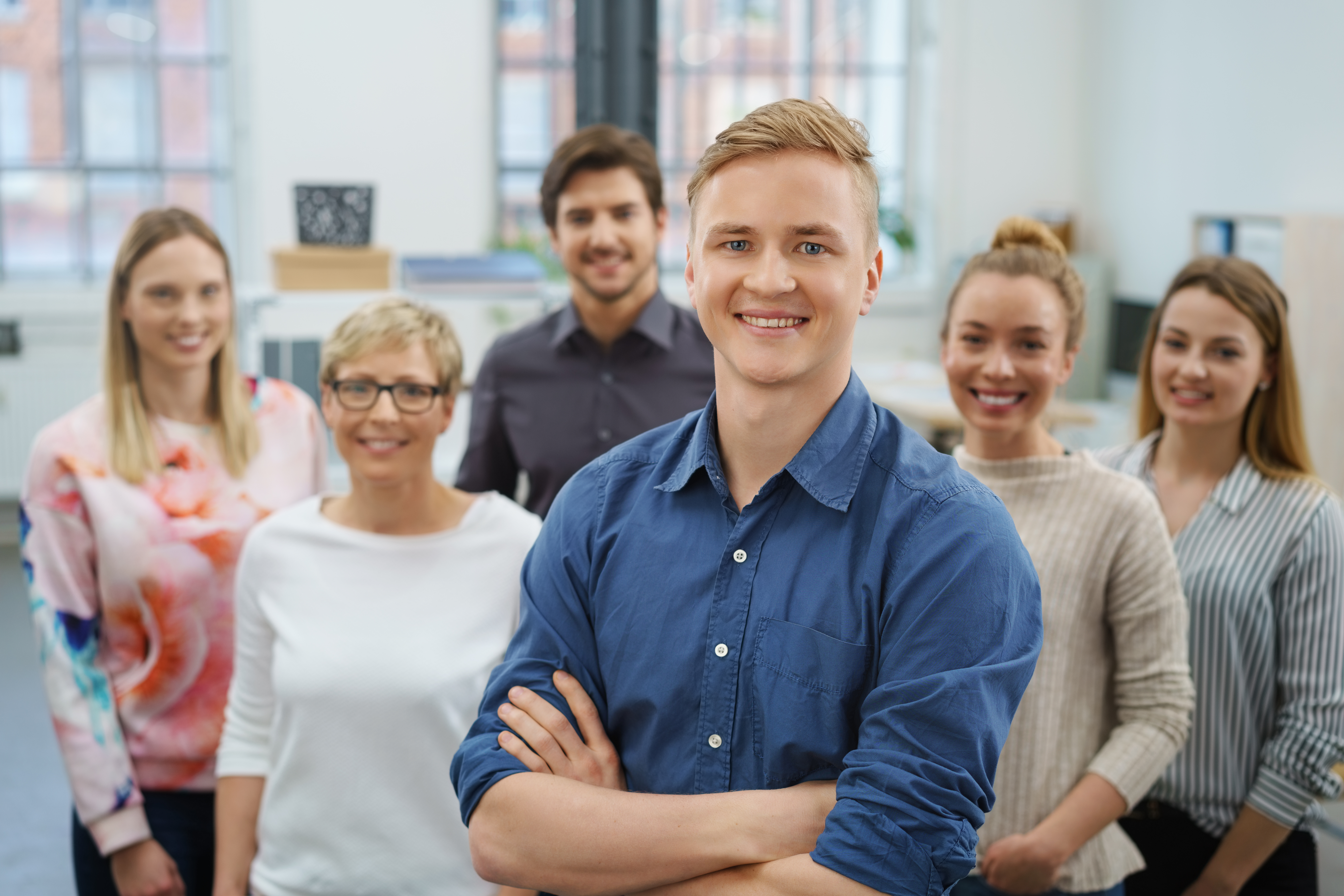 Team von sechs Leiharbeitern im Büro freut sich über die Vorteile von Zeitarbeit, junger blonder Mann im Vordergrund.